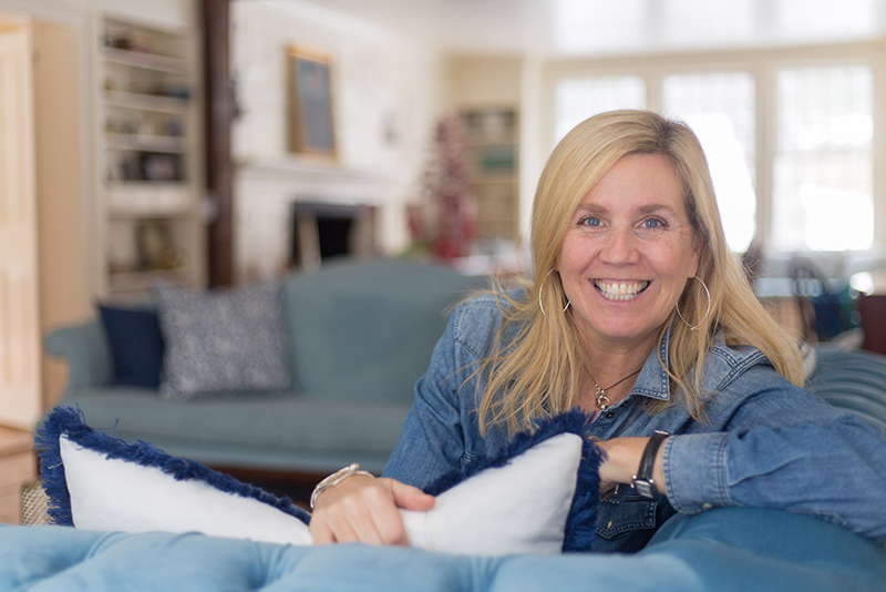 Kasey Mathews smiling wide as she turns to look over the side of a blue couch