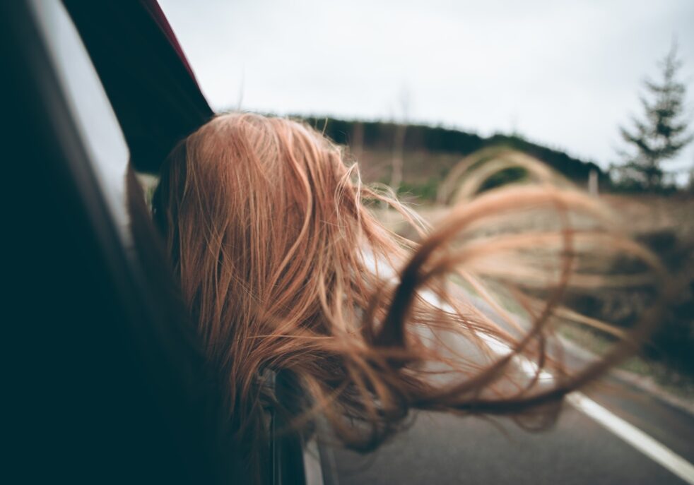 woman with head out care window driving down smooth road after changes