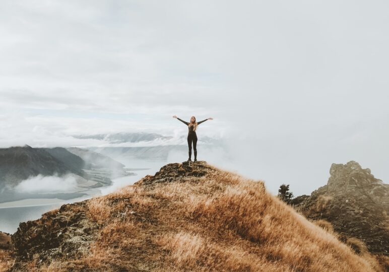 strong woman standing on mountain with arms in the air